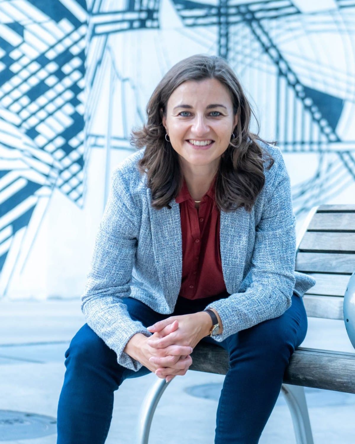 Karen Knab smiling and leaning forward on a bench, hands clasped, facing the camera