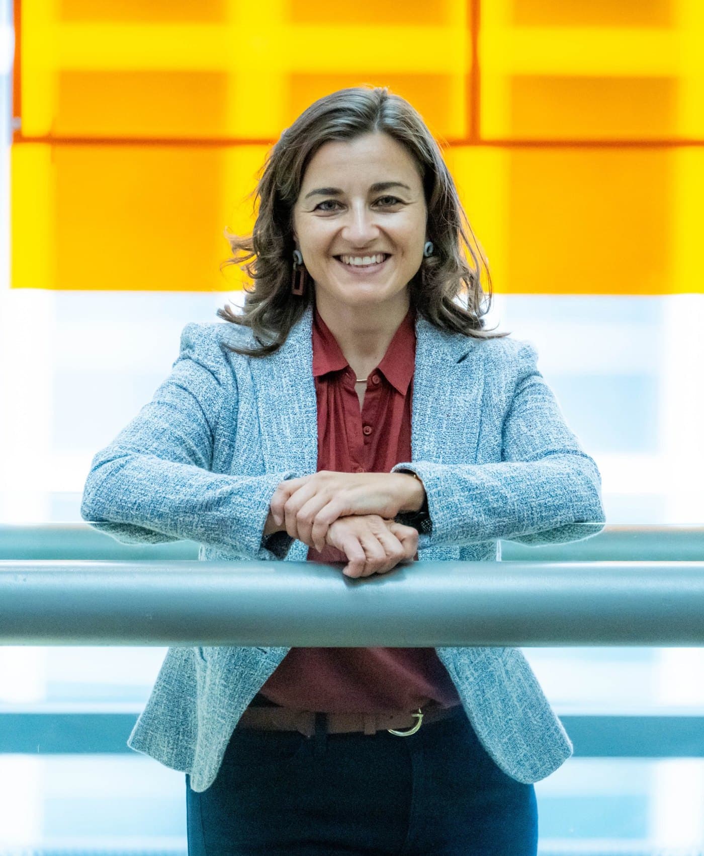 Karen Knab smiling, leaning on a railing in front of a bright orange and white glass wall